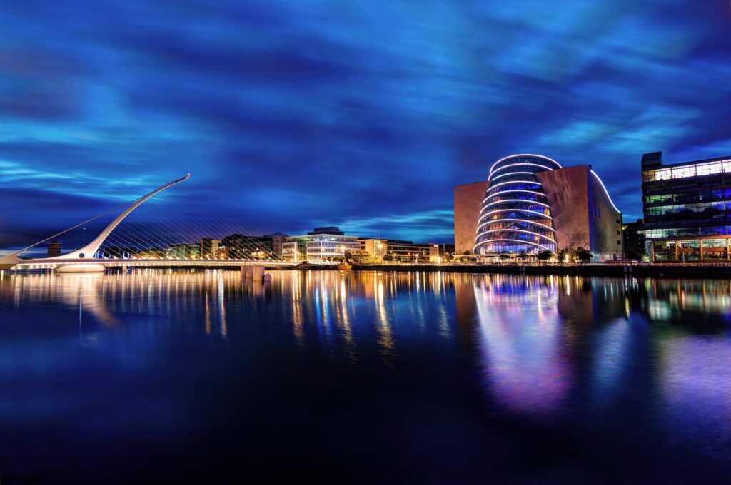 The harp-shaped Samuel Beckett Bridge and the illuminated tilted glass atrium of the Convention Centre Dublin glow at blue hour